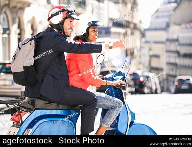 Happy young business couple riding motor scooter in the city, Lisbon, Portugal