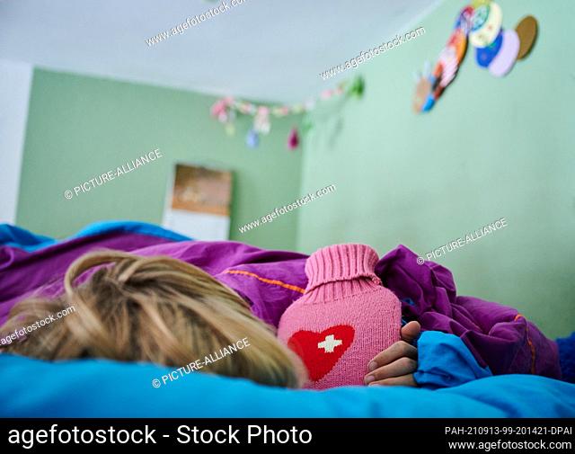 ILLUSTRATION - 11 September 2021, Berlin: A child lies in bed with a hot water bottle. Photo: Annette Riedl/dpa. - Berlin/Berlin/Germany