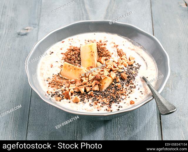 Close up view of overnight oats in bowl with banana, LSA, chia seeds, almond and honey on gray wooden table background. Healthy breakfast oatmeal recipe idea