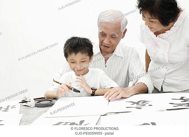 Couple and young boy indoors painting Chinese letters