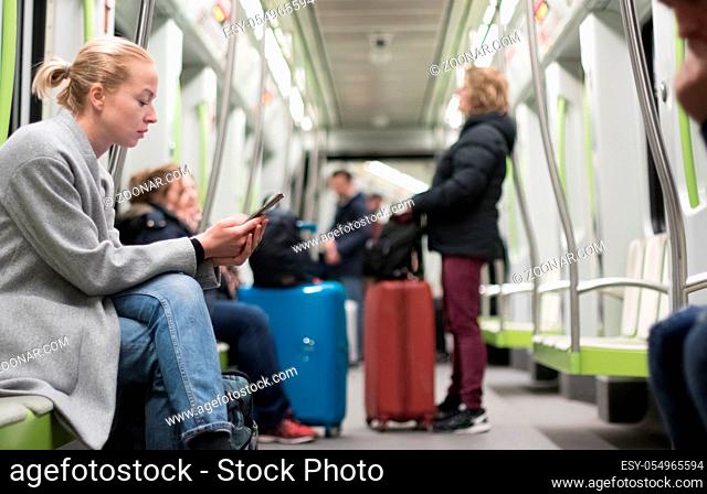 Beautiful blonde caucasian woman wearing winter coat reading on the phone while traveling by metro. Public transportation concept