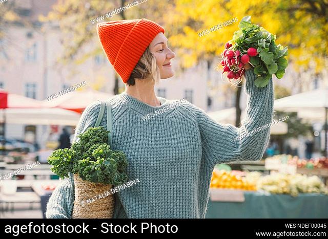 Smiling woman wearing sweater looking at radish at market