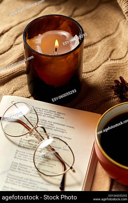 book, glasses, coffee and candle on warm blanket