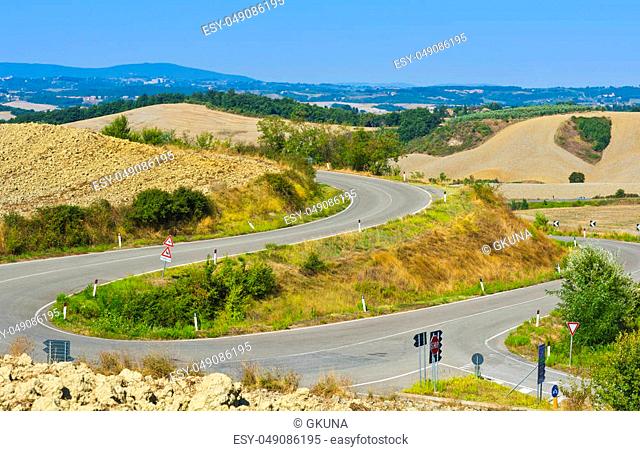 Plowed sloping hills of Tuscany in the autumn. Rural landscape with field after harvest. Asphalt road between plowed fields in Italy