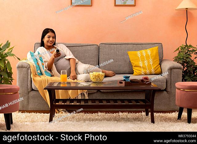 Happy pregnant woman watching TV while relaxing on sofa at home
