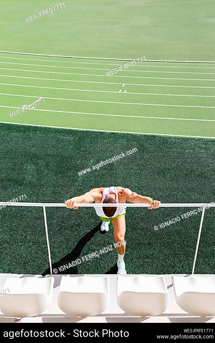 Athlete doing warm exercise by railing on sports field