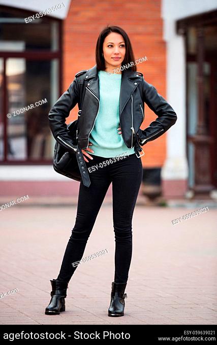 Young fashion woman with backpack walking in city street Stylish female model in black leather jacket outdoor