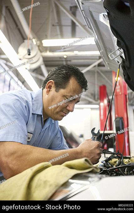Hispanic mechanic leans into an engine of a car he is working on in an auto repair shop
