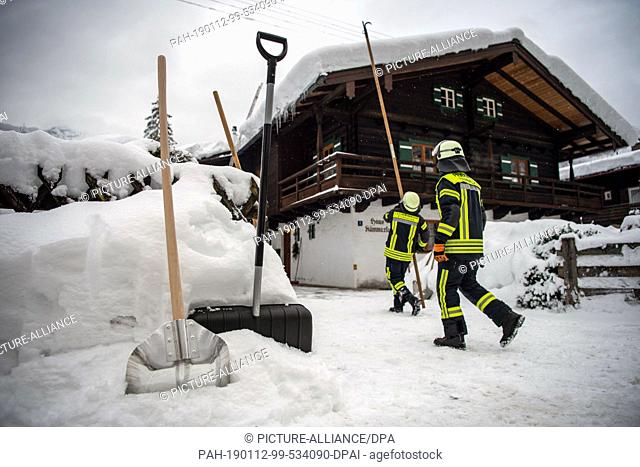 12 January 2019, Bavaria, Berchtesgaden: Shovels are standing in front of firefighters who are just clearing a roof of snow