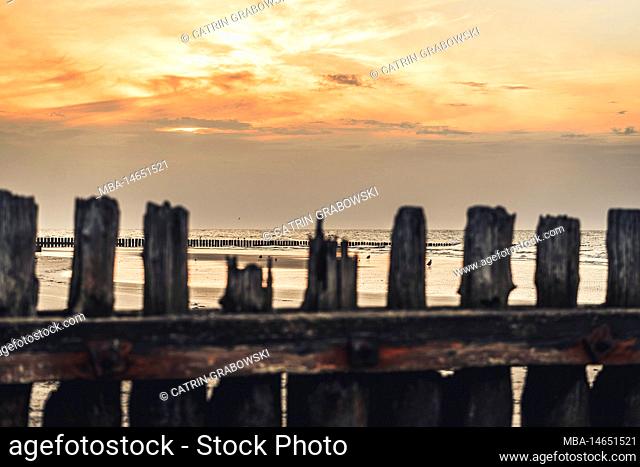 Sunset on the northern beach of the North Sea island of Norderney, blurred groynes in the foreground