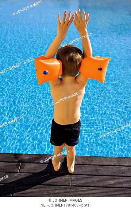 Boy wearing inflatable armbands on edge of swimming-pool