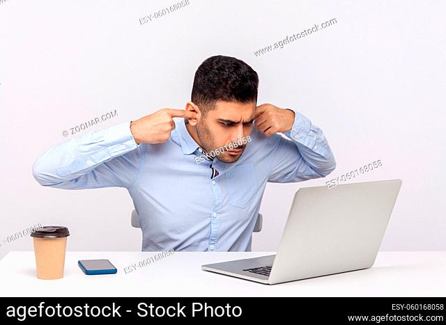 Don't want to hear you. Irritated businessman sitting office workplace, closing ears while talking video call on laptop, looking annoyed by unpleasant job...