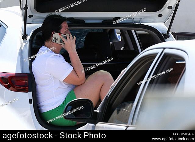 RUSSIA, REPUBLIC OF CRIMEA - JULY 17, 2023: A woman speaks on her phone while sitting in the trunk of a car by the Kerch Strait ferry line