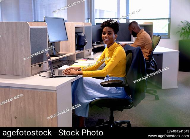 Portrait of smiling young african american female advisor using laptop at desk in modern workplace