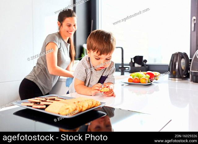 Kind als Naschkatze in der Küche beim Kekse naschen mit Mutter im Hintergrund