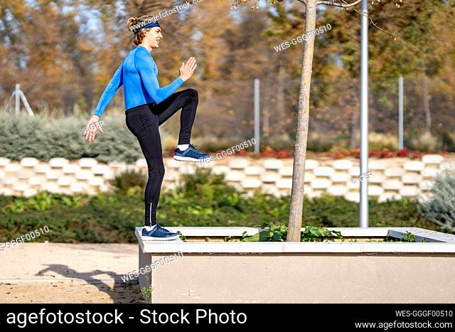 Young male sportsperson exercising on retaining wall in public park on sunny day