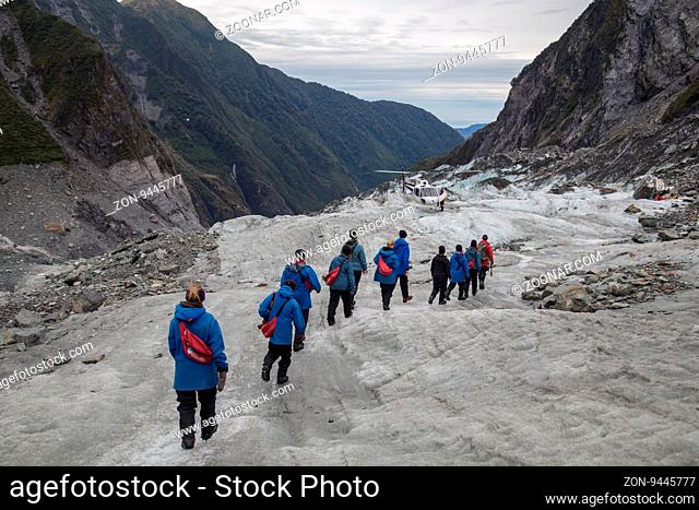 Franz Josef, New Zealand - March 22, 2015: A group of tourists hiking towards a helicopter on Franz Josef Glacier