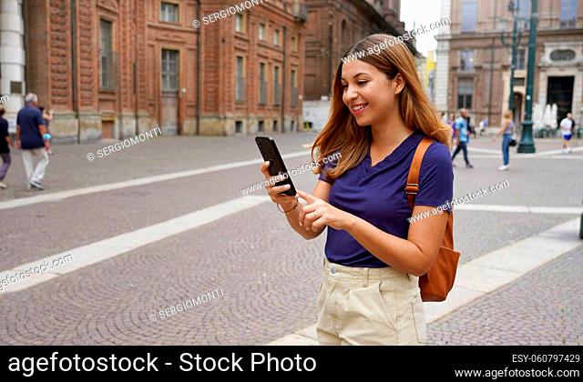 Beautiful university student female walking in city street typing on telephone