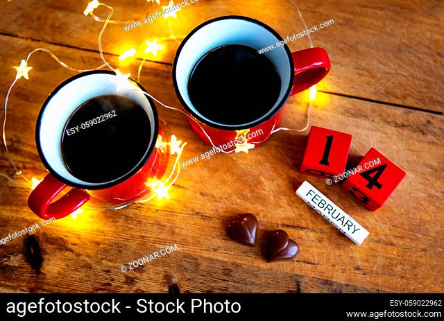 Two cups of coffee in red cups on a background of chocolate canfet. Postcard with date and month. Valentine's Day Morning Surprise