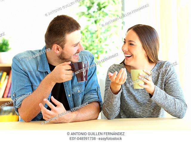 Front view of a casual couple talking looking each other during breakfast in a table of the living room at home