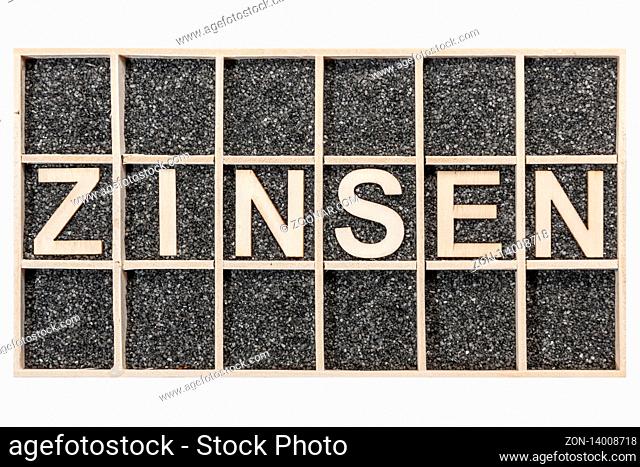 Plywood letters arranged in a collecting box with black decorative sand representing the word ZINSEN in top view isolated on white