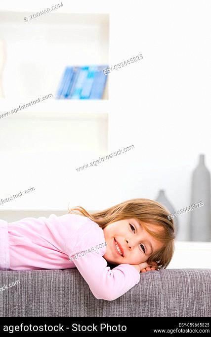 Happy little girl in pink dress, lying on couch, smiling