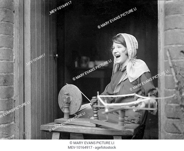 A young girl worker using a spinning wheel to spin thread for pillow lace, Honiton, Devon, England