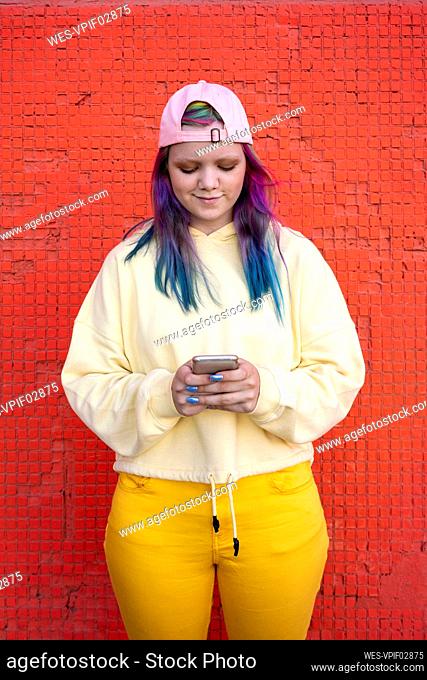 Portrait of young woman with dyed hair using smartphone in front of yellow wall