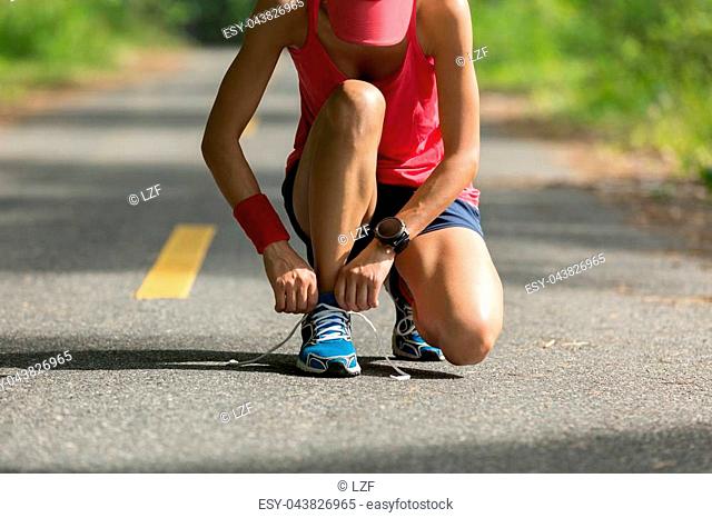 young fitness woman runner tying shoelace before run on sunset beach