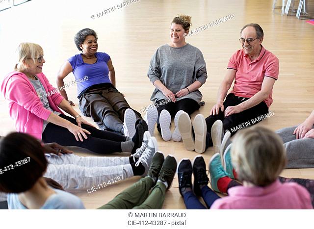 Instructor and active seniors stretching legs in circle in exercise class