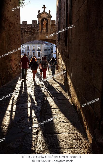 Caceres, Spain - July 1, 2017: Tourists walking under Star Arch or Arco de la Estrella, Caceres. Sunset light