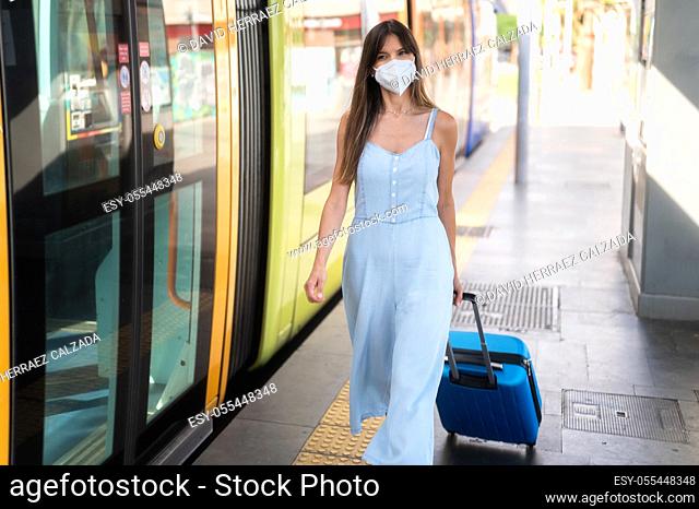 Woman in protective face mask standing on the railway station near the train with her suitcase. Traveling during the pandemic. New normal