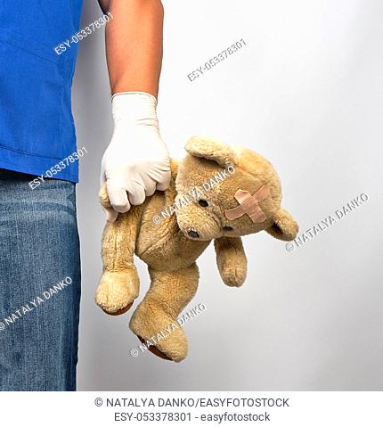 doctor in blue uniform and white latex gloves holding a brown teddy bear, pediatrics concept, copy space