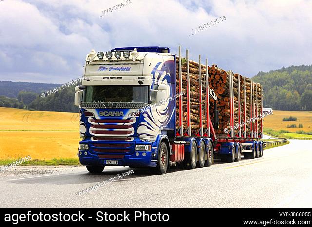Customized Scania logging truck of Kuljetusliike Niko Gustafsson pulls log load uphill on highway in rainy weather. Salo, Finland