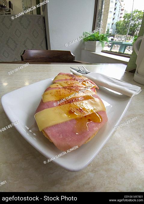 Ham toast with sliced cheese sprinkled with Pimenton de la Vera. Knife and fork wrapped in a paper napkin