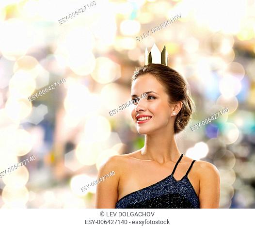 people, holidays, royalty and glamour concept - smiling woman in evening dress wearing golden crown over lights background