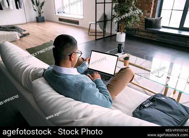 Freelancer using laptop sitting on sofa in living room at home
