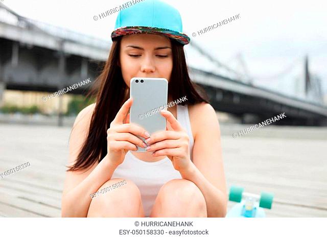 Pretty young white girl taking photo with big phablet smartphone with dual rear camera. Attractive female model, trendy mobile phone