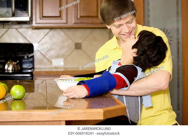 Father helping disabled son putting fruit into bowl in the kitchen. Son has cerebral palsy