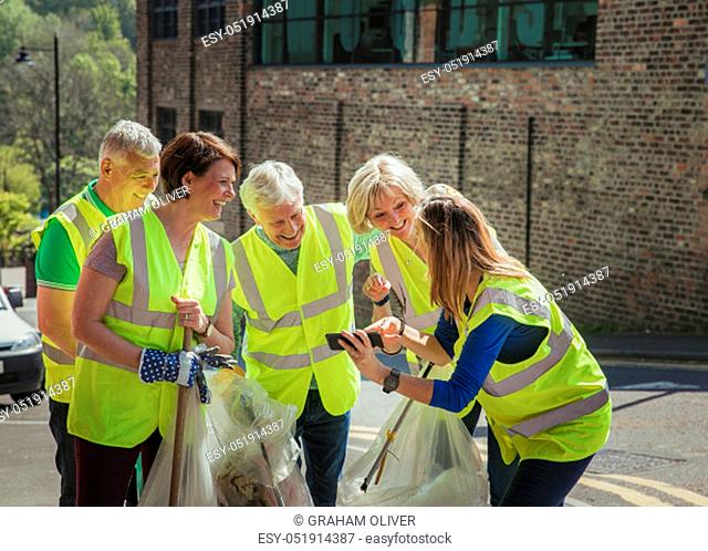A group of five people taking a selfie. They are wearing high visibility jackets and are participating in a city clean-up