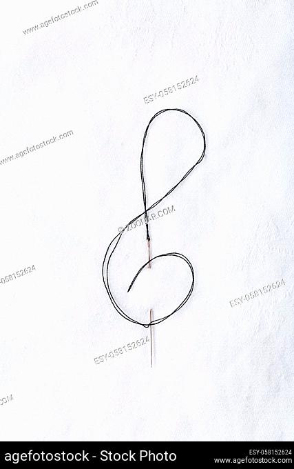 Macro of sewing needle in white fabric in violin key shape. Concept of handcraft and art