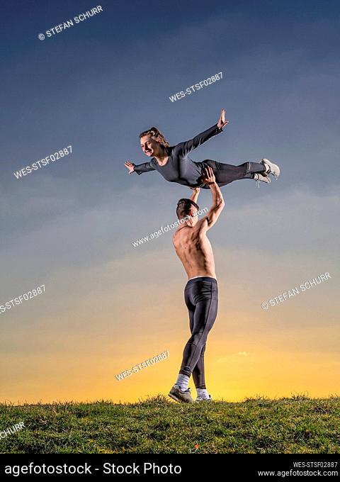 Man lifting woman while doing acrobats during sunset