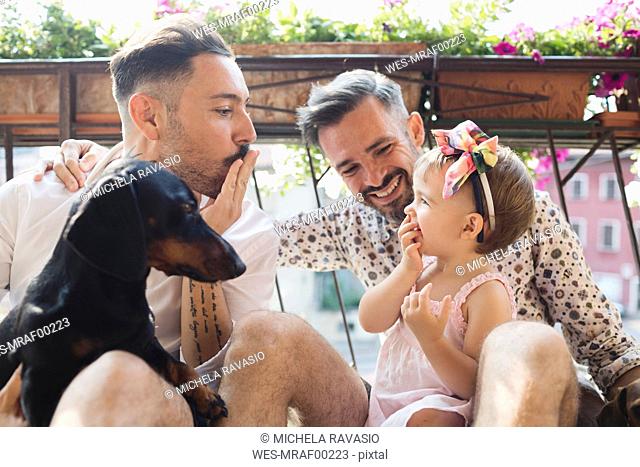 Happy gay couple with daughter and dog on balcony