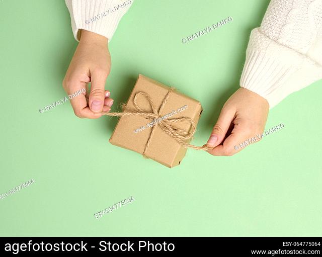 Female hands holding a gift box on a green background. View from above