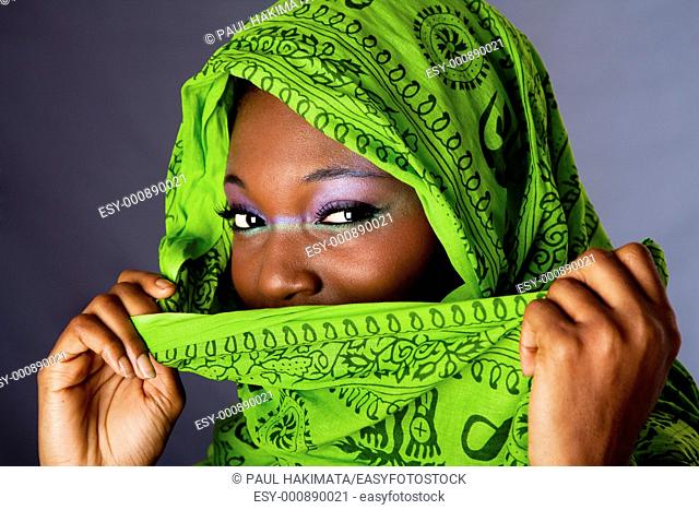 The face of an innocent beautiful young African-American woman covering her mouth with green headwrap and purple-green makeup, isolated