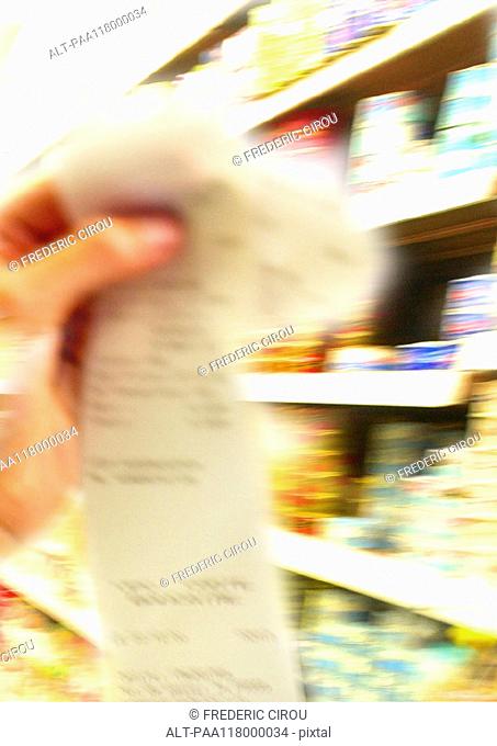 Hand holding receipt, supermarket shelves in background, blurred