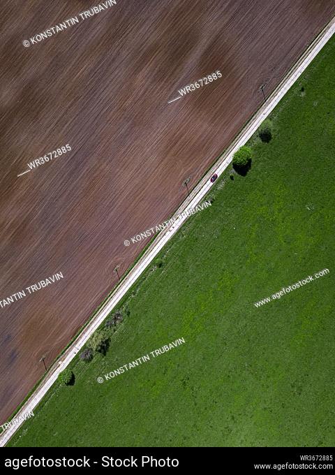 Aerial view of car driving along countryside road stretching between green and brown field