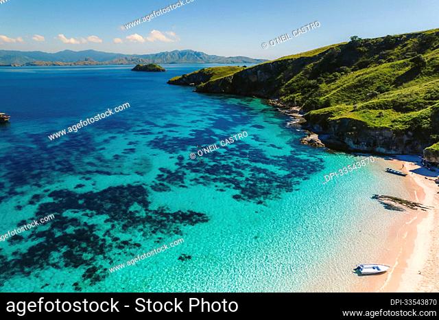 Aerial view a motor boats beached on the shore of a pink sand beach and people enjoying the seaside along the shore of Padar Island in Komodo National Park;...