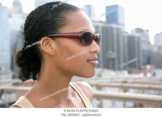 Young woman wearing sunglasses, skyline in the background, portrait