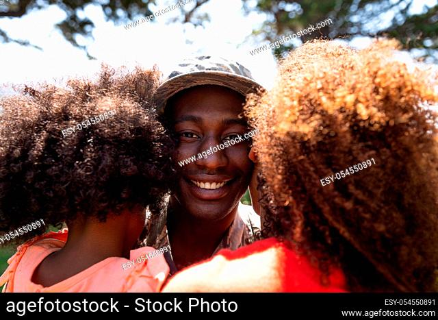Over shoulder view of a young adult African American soldier embracing his young daughter and his young mixed race female partner, seen close up from behind